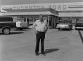 Photograph: [Howard Thornton standing in front of a Ford dealership]