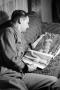 Photograph: [Photograph of a man looking at a magazine on a couch, 2]
