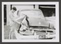 Photograph: [Photograph of a teenage boy pointing towards a wrecked automobile]