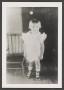 Photograph: [Photograph of a little girl standing next to a chair]