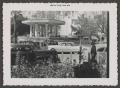 Photograph: [Photograph of automobiles parked on the street by a crowded pavilion]