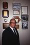 Primary view of [Dr. Thomas Tolbert stands in front of framed mementoes]