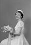 Photograph: [Frieda Warrington in a lace dress, holding a bouquet and smiling]