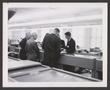 Photograph: [A group of men standing together and talking in an office]