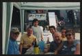 Primary view of [7 people sitting under a stripped tent by a wooden deck: Lone Star Ride 2003 event photo]