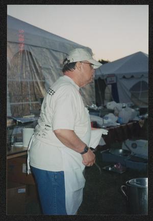Primary view of object titled '[Volunteer in a white apron helping cook: Lone Star Ride 2003 event photo]'.
