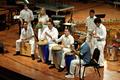 Photograph: [A group in white playing percussion instruments and singing]