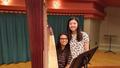 Photograph: [Two girls posing next to a harp and a music stand]