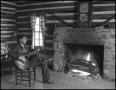 Photograph: [Young man playing guitar by the fireplace]