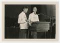 Photograph: [Two unidentified men wearing Container Store shirts stand at a podiu…