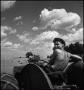 Photograph: [Young man driving a tractor and looking back behind him]