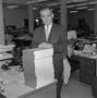 Photograph: [John L. Carter standing next to a stack of books, 3]