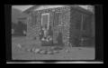 Photograph: [Irene Williams standing outside of her home with three children]