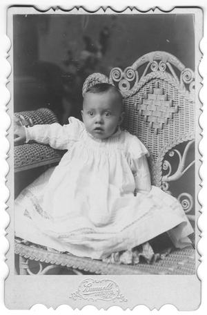 Primary view of object titled '[Unidentifed baby in white dress sits in wicker chair]'.