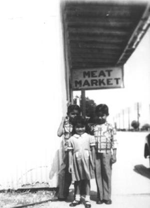 Primary view of object titled '[Photograph of three children standing by a "Meat Market" sign]'.