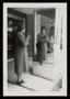 Photograph: [Sheila Emery Allen looking at her reflection in mirror near storefro…