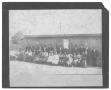 Primary view of [Group Portrait in Front of a Small Wood-Slatted Building]