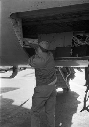 Primary view of object titled '[An airport worker putting cases in the luggage compartment of a plane]'.