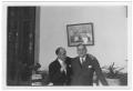 Primary view of [George Alfred Hill, Jr. with unidentified man in room with potted plants]