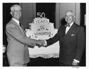 Primary view of object titled '[Abe and Joe Weingarten shaking hands in front of 50 years of Weingarten's cake]'.