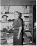 Photograph: [Woman in boutique standing next to hat display]