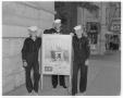 Primary view of [Three young men in navy uniforms standing next to recruitment poster]
