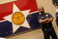 Photograph: [A Police Officer Stands Beside a Framed City of Dallas Flag, Looking…