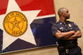 Photograph: [A Police Officer Stands Beside a Framed City of Dallas Flag and Look…