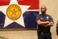 Photograph: [A Police Officer Stands Beside a Framed City of Dallas Flag]