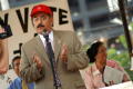 Photograph: [Hector Flores speaking while wearing suit and red hat]