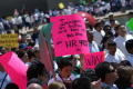 Photograph: [Protesters carry brightly colored signs]