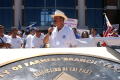 Photograph: [Man in a hat with a microphone addressing the crowd ]