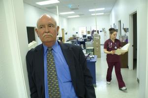 Primary view of object titled '[Eddy Herrera leans against doorway with clinic staff member in the background]'.