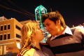 Photograph: [Young man and woman with green lit skyscraper in background]