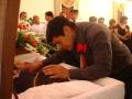Photograph: [Young man leaning over casket with mourners in background]