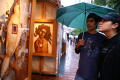 Photograph: [Young man and woman under umbrella, looking at artwork]