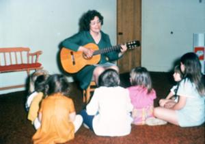 Primary view of object titled '[Children watching woman with guitar in Emily Fowler Library]'.