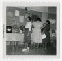 Photograph: [Women Looking at Display with Dishes, Linens, and Dolls]