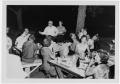 Photograph: [People Eating at Night on Outdoor Picnic Tables]
