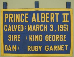 Primary view of object titled '[Blue canvas and yellow felt banner that states: "PRINCE ALBERT II CALVED: MARCH 3, 1951]'.