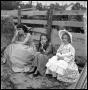 Photograph: [A Woman and Two Girls Sitting by a Fence]