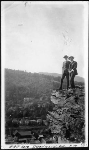 Primary view of object titled '[Two men standing on the edge of a rock cliff overlooking a city]'.