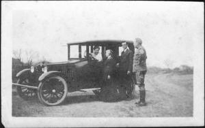 Primary view of object titled '[Woman sitting in an automobile with three people standing nearby]'.