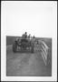 Photograph: [Three tractors passing through a wooden gate at the George Ranch]