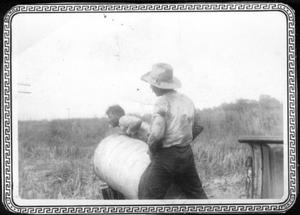 Primary view of object titled '[Two men lifting a steel drum in a field at the George Ranch]'.
